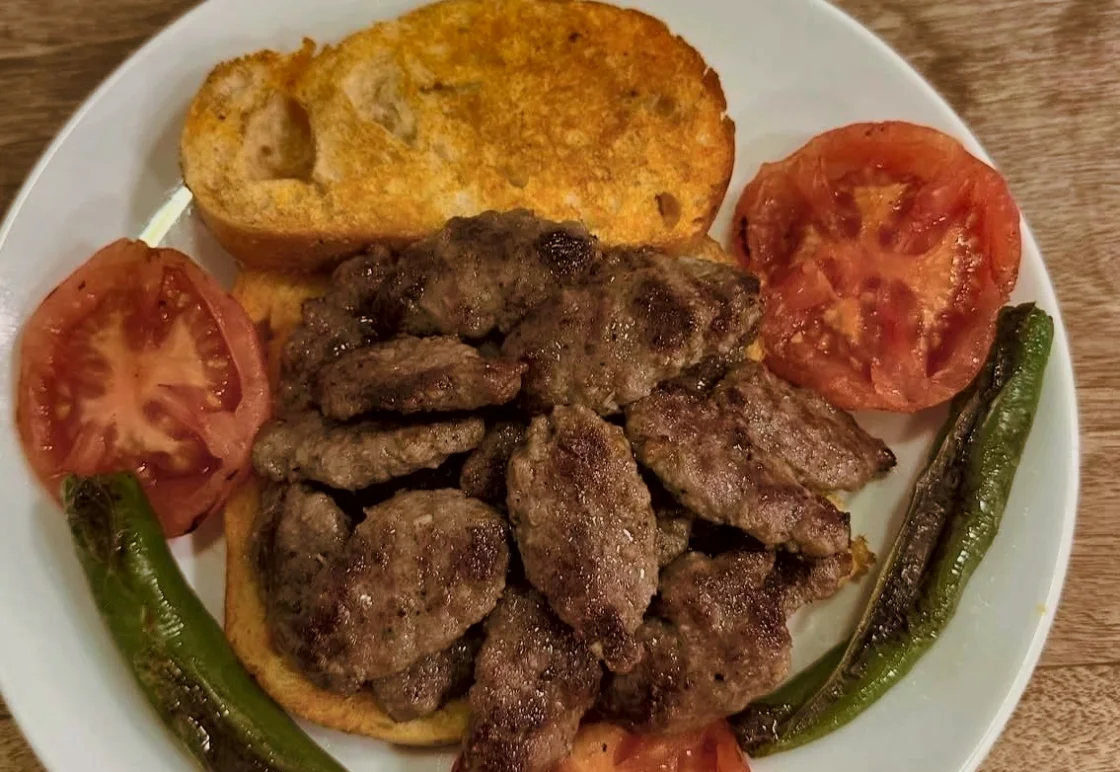 Sosuyla ıslanmış ekmek üstünde ıslama köfte, domates ve közlenmiş biber